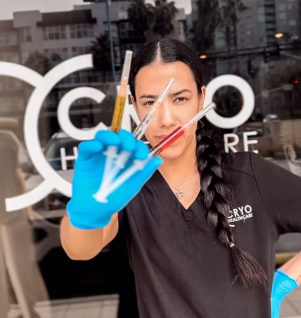 Woman holding three different vitamin injections in front of the Cryohealthcare logo on the building